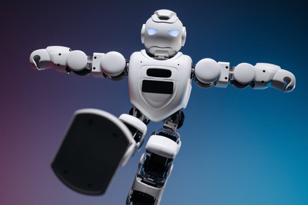 Kleiner weißer Roboter mit blauen Augen, springt dynamisch mit ausgestreckten Armen und Bein vor blau-violettem Hintergrund.