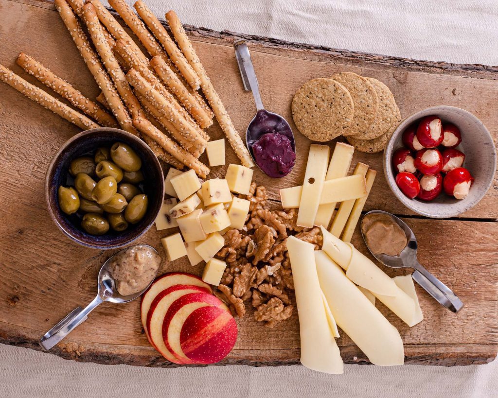 Rustikale Brettljause auf Holzbrett mit Käse, Obst, Nüssen und Dips aus Unverschwendet-Produkten fein angerichtet.