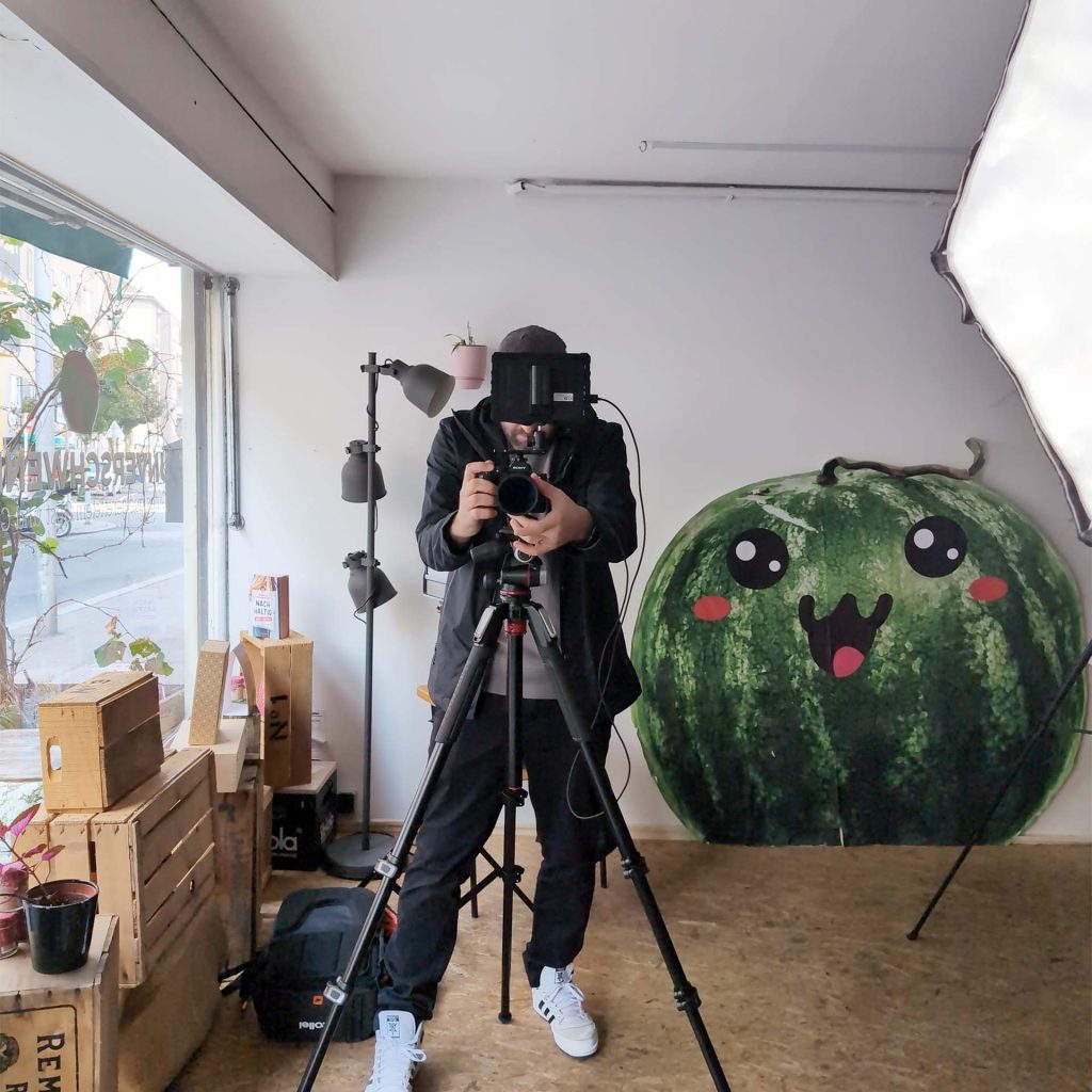 Markus bei der Content-Produktion im Unverschwendet-Atelier mit Kamera und lächelnder Wassermelonen-Figur.