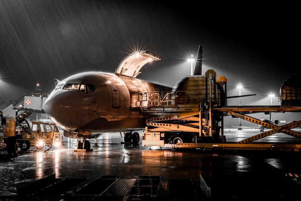 Frachtflugzeug wird nachts bei Regen am Flughafen Linz entladen, starke Kontraste durch künstliche Beleuchtung