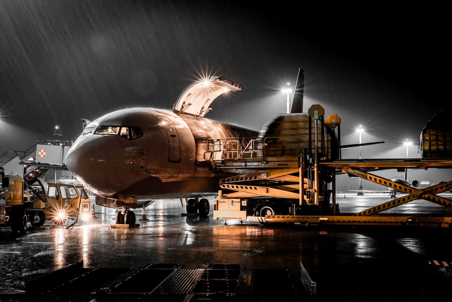 Frachtflugzeug wird nachts bei Regen am Flughafen Linz entladen, starke Kontraste durch künstliche Beleuchtung