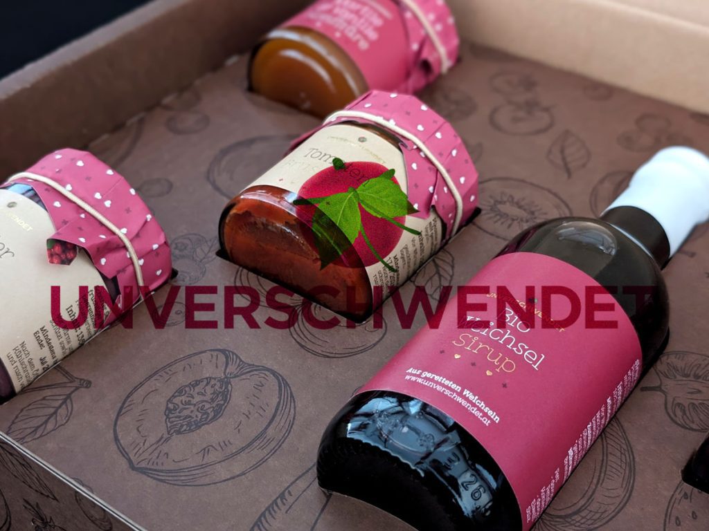 Nahaufnahme eines Produktsets von Unverschwendet mit Sirup und Konfitüre aus geretteten Früchten in dekorativer Verpackung.
