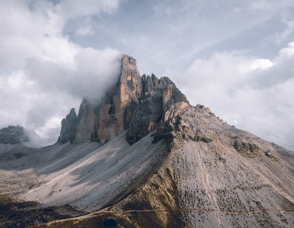 Debug 19 Felsige Bergspitze ragt aus Nebel in den Himmel, steinige Hänge mit sichtbaren Pfaden durchziehen die karge Landschaft.